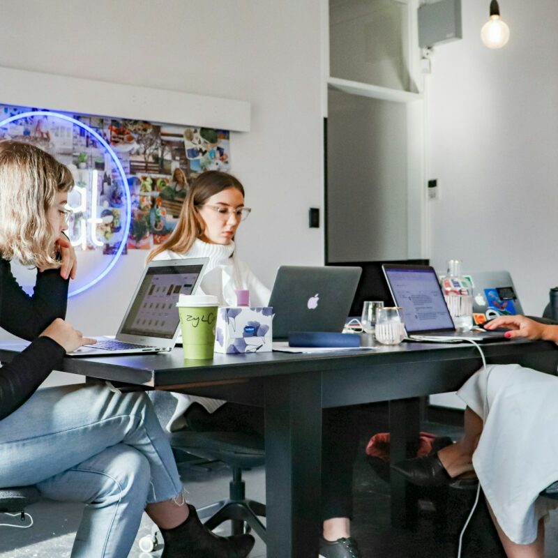 3 women sitting on chair in front of table with laptop computers